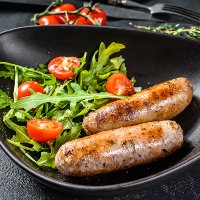 Grilled sausages with tomato and arugula salad. BBQ meat recipe. german food recipe. Black background. Top view.